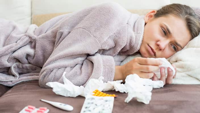 Sad woman with tissue and medicines lying on bed