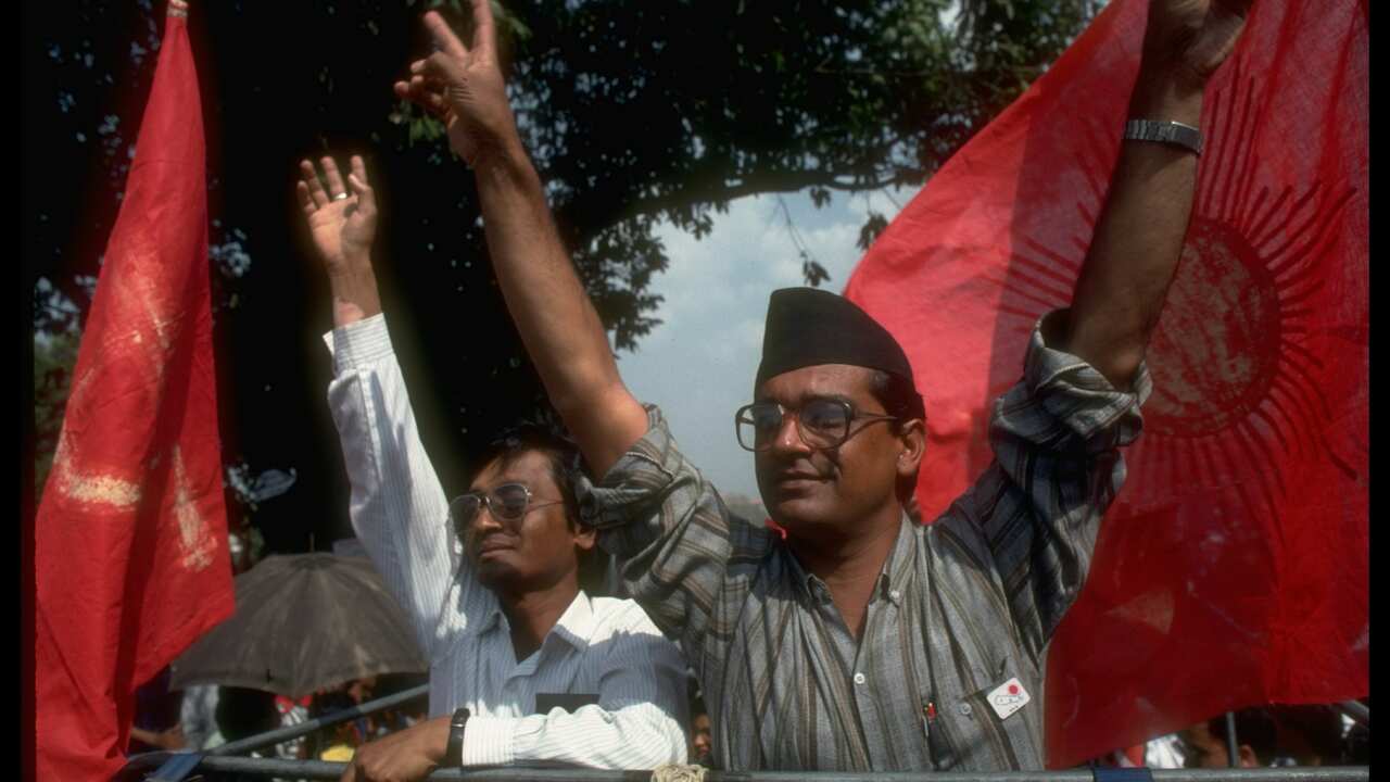 1991 photo of the then Communist Party of Nepal General Secretary Madan Bhandari (L), veeing fingers, on stump, framed by CPM UML red flags, candidate in first free election in 30 yrs.