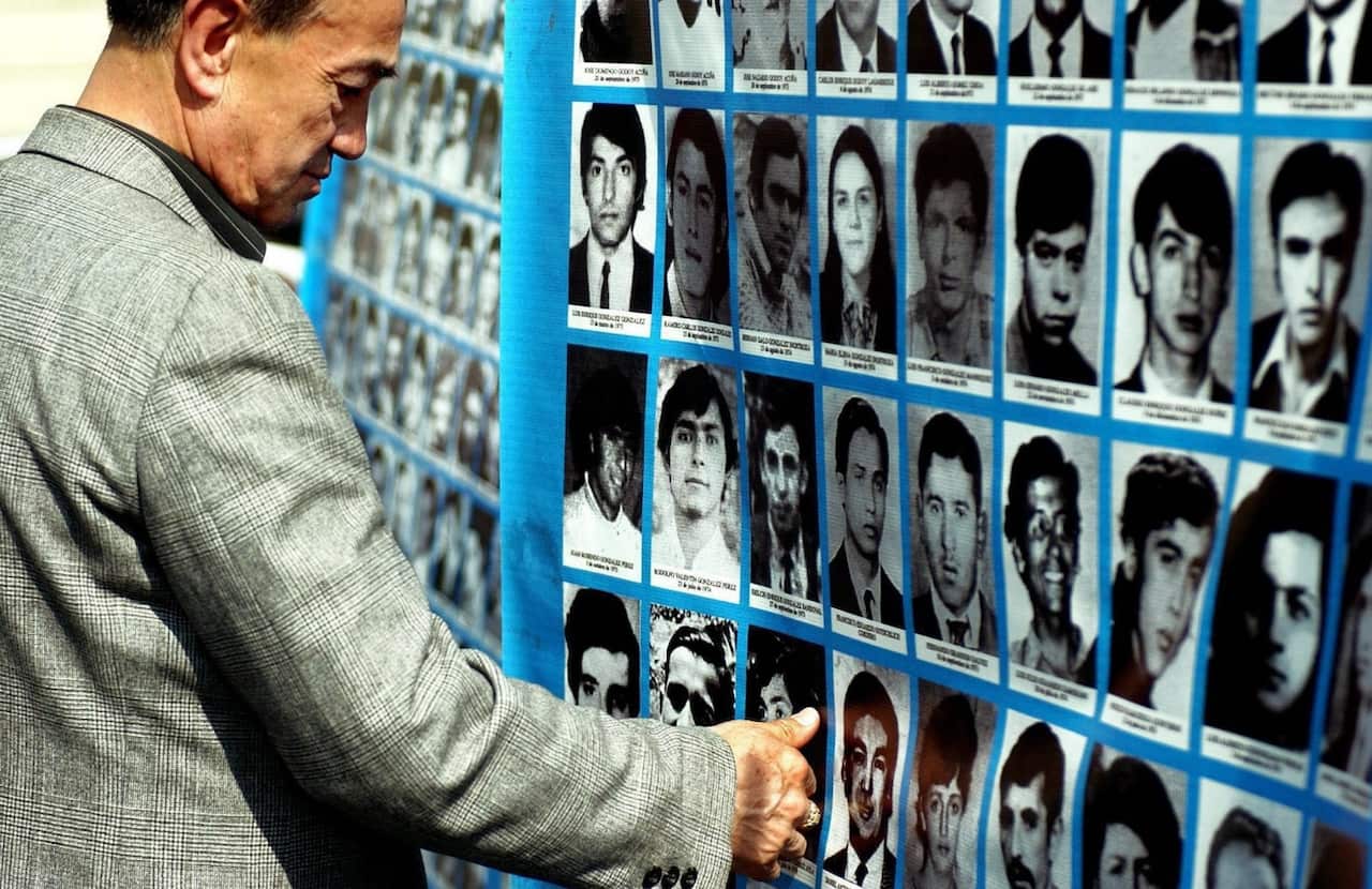 In this 2004 file photo, members of families of the disappeared and detained look at images of their loved ones in the main square of Santiago, Chile.