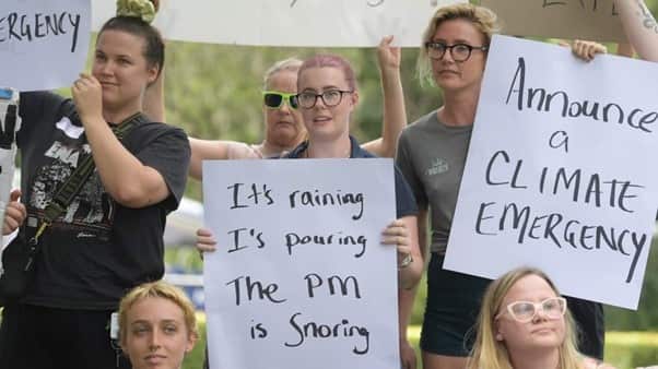 Local residents hold signs as they wait for Prime Minister Scott Morrison during a visit to the Emergency Operations Centre in Lismore.