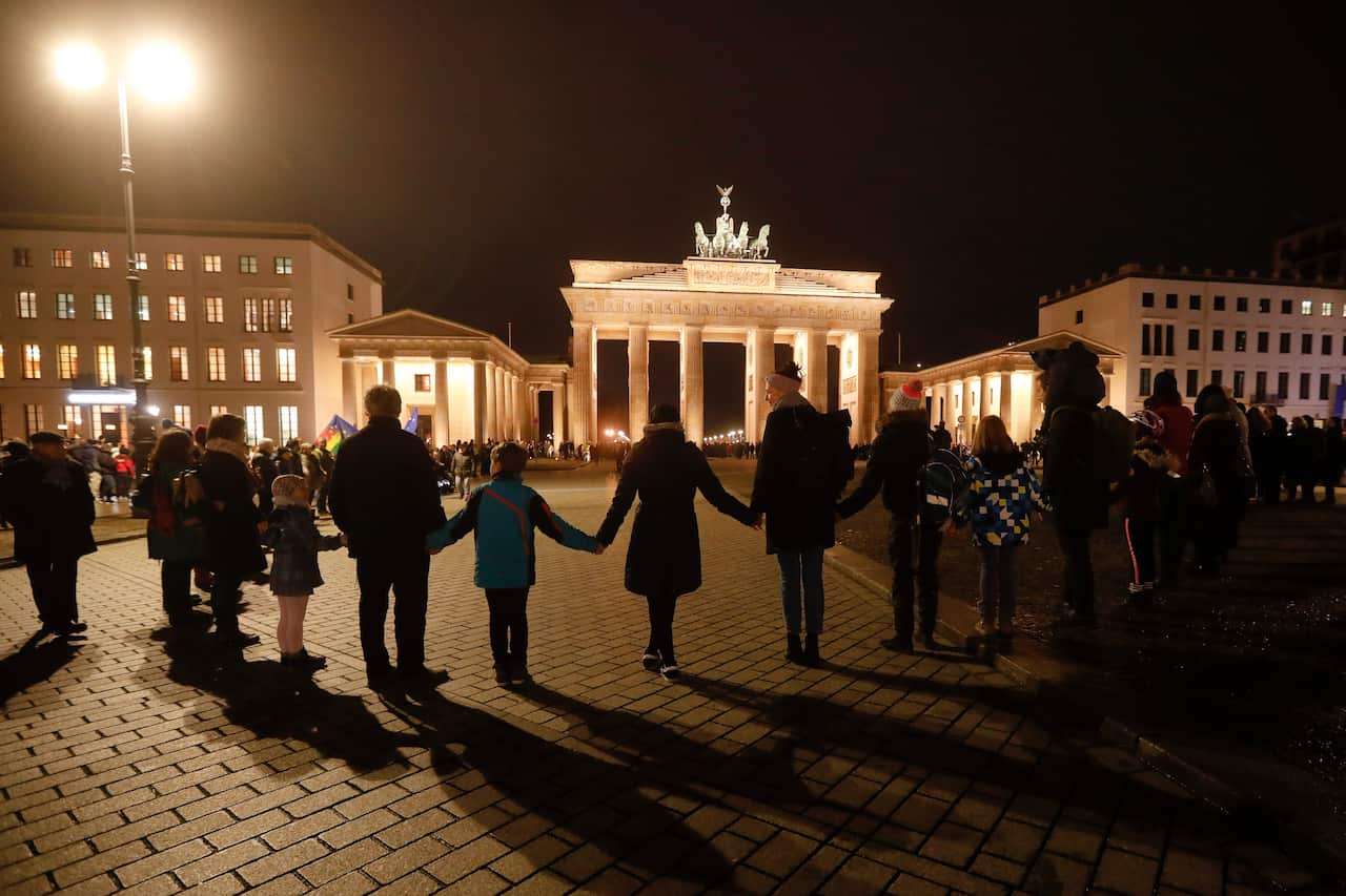 People stand for a human chain during a vigil for victims of last night's shooting in the central German town Hanau, in front of the Brandenburg Gate in Berlin.