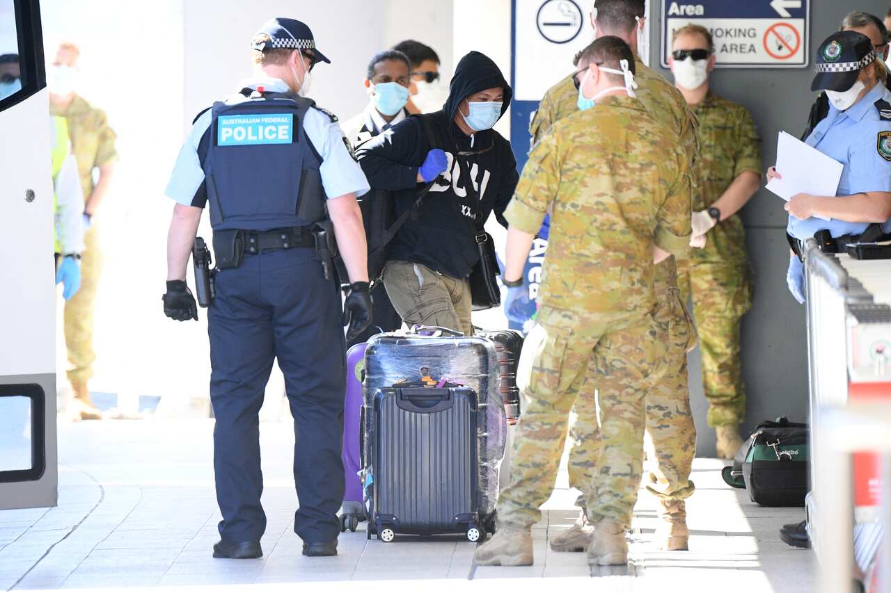 Army soldiers and police officers assist returning travellers as they make their way into quarantine.