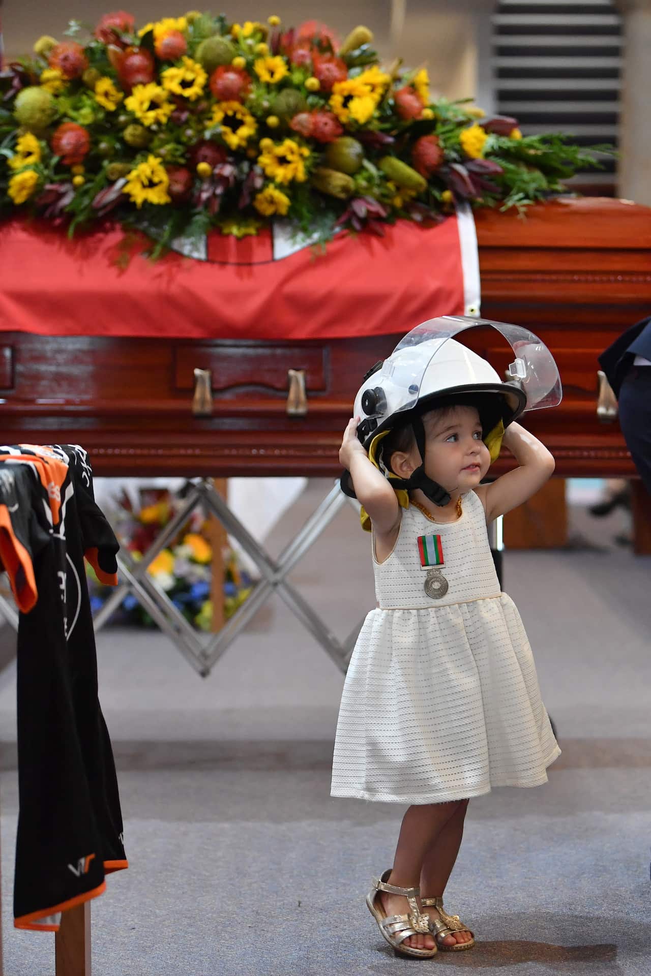 Charlotte O'Dwyer, the young daughter of Rural Fire Service volunteer Andrew O'Dwyer stands in front of her fathers casket wearing his helmet.