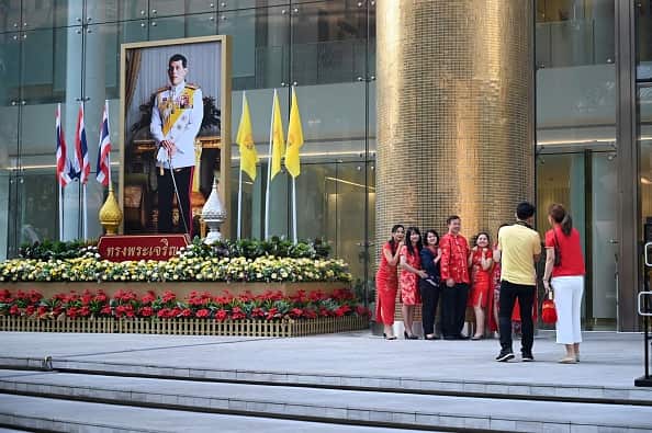 A group of people wearing colourful outfits pose for picture next to a large portrait of Thai King Maha Vajiralongkorn in Bangkok.