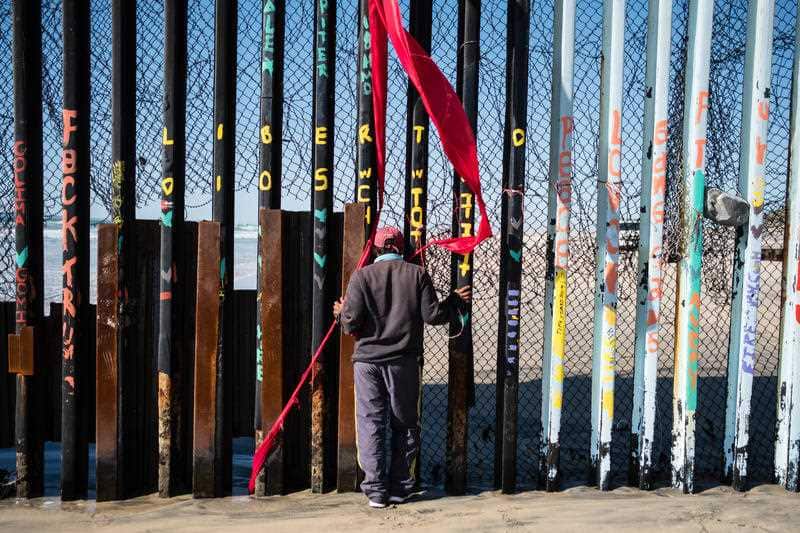 A boy looks through the fence at border patrol before slipping through the fence in efforts to seek asylum in the United States.