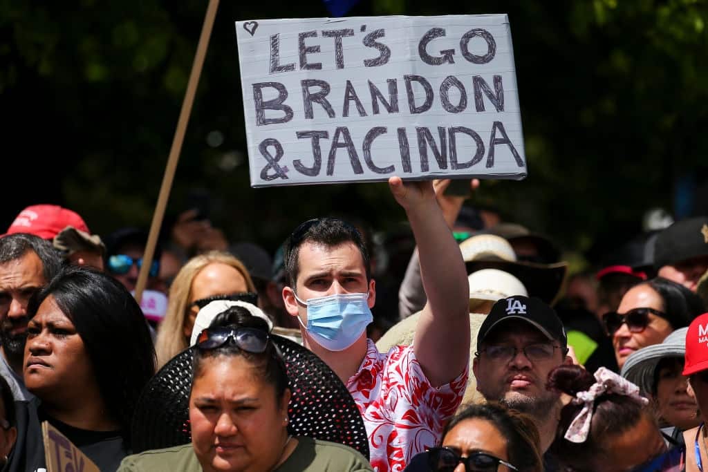 A man holds a 'Let's go Brandon and Jacinda' sign at a COVID-19 protest in Wellington