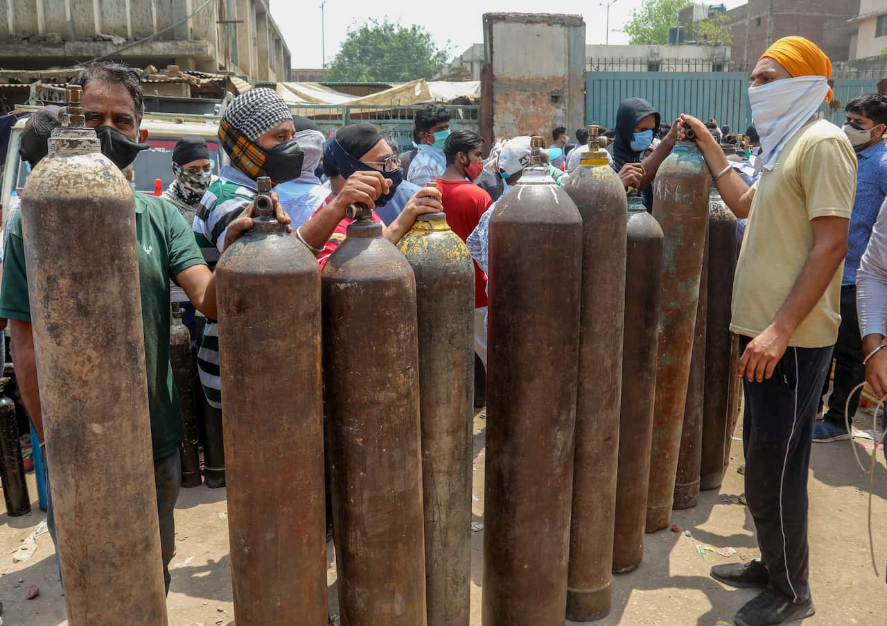 Family members of COVID-19 patients hold empty oxygen cylinders for refilling at Narayana Industrial area in New Delhi. 
