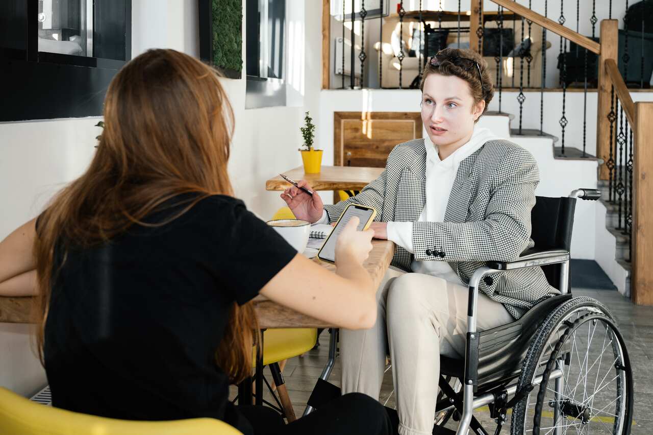 Woman in wheelchair communicating with female colleague in cafe