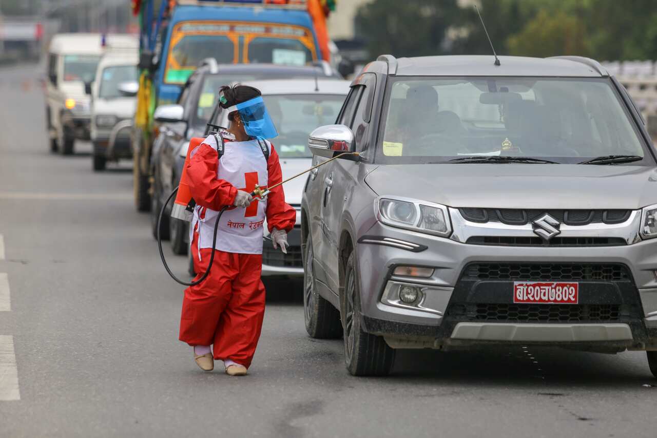 A member of the Red Cross Society sprays disinfectants onto a vehicle at a check-point along Kathmandu and Bhaktapur district border.