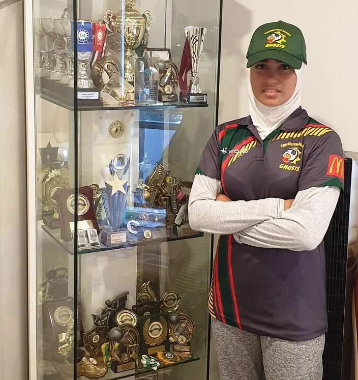 Zoha standing next to the family's collection of trophies won in cricket.