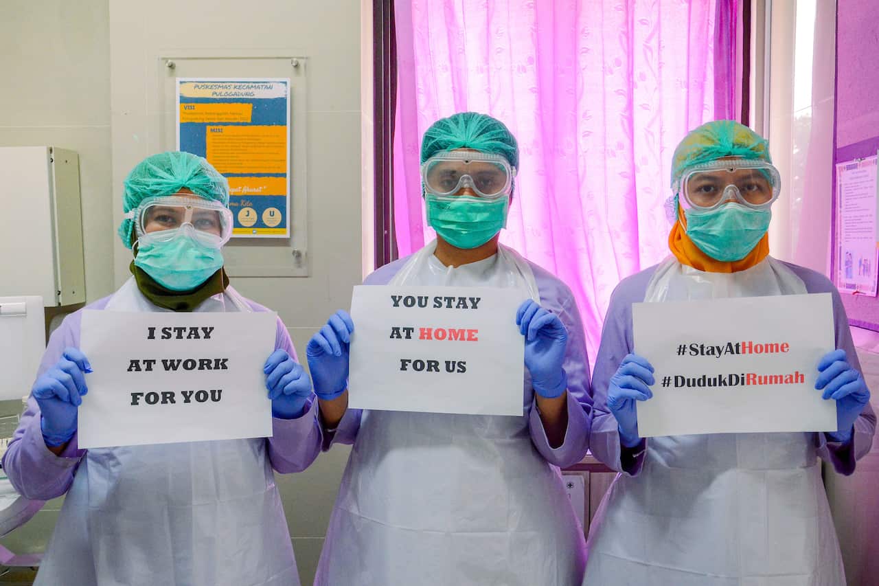 Medical workers wearing a face mask holds a 'Stay at Home' poster at a medical center in Jakarta, Indonesia.