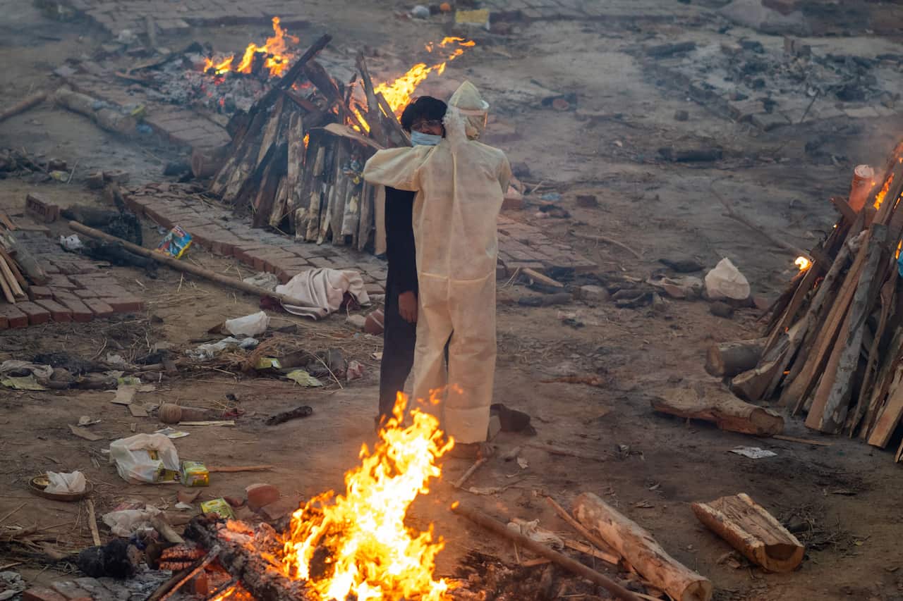 Family members embrace amid burning pyres of victims who lost their lives due to COVID-19 at a cremation ground in New Delhi on 26 April, 2021. 