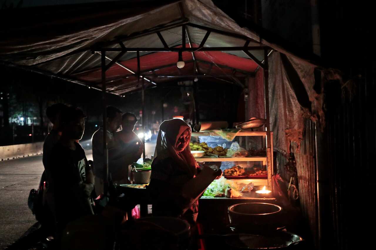 A vendor is illuminated by candle light as she serves customer.
