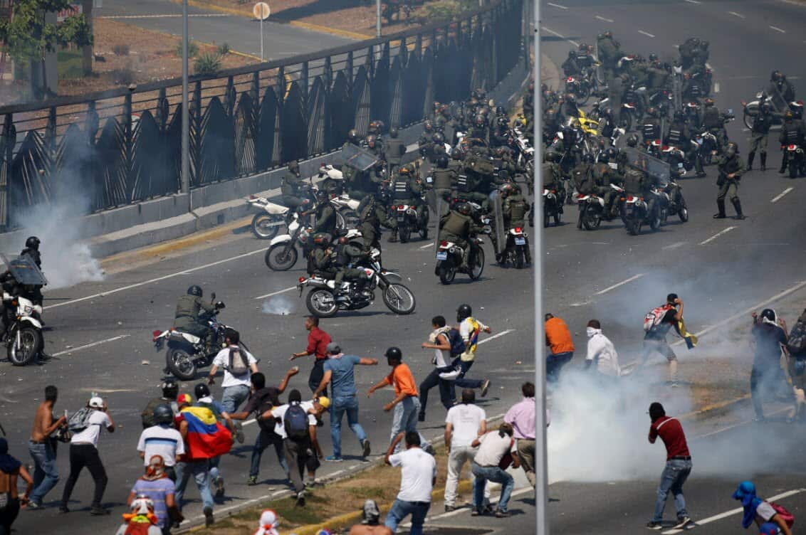 Opponents to Venezuela's President Nicolas Maduro confront loyalist Bolivarian National Guard troops firing tear gas at them outside La Carlota military airbase in Caracas (AAP)