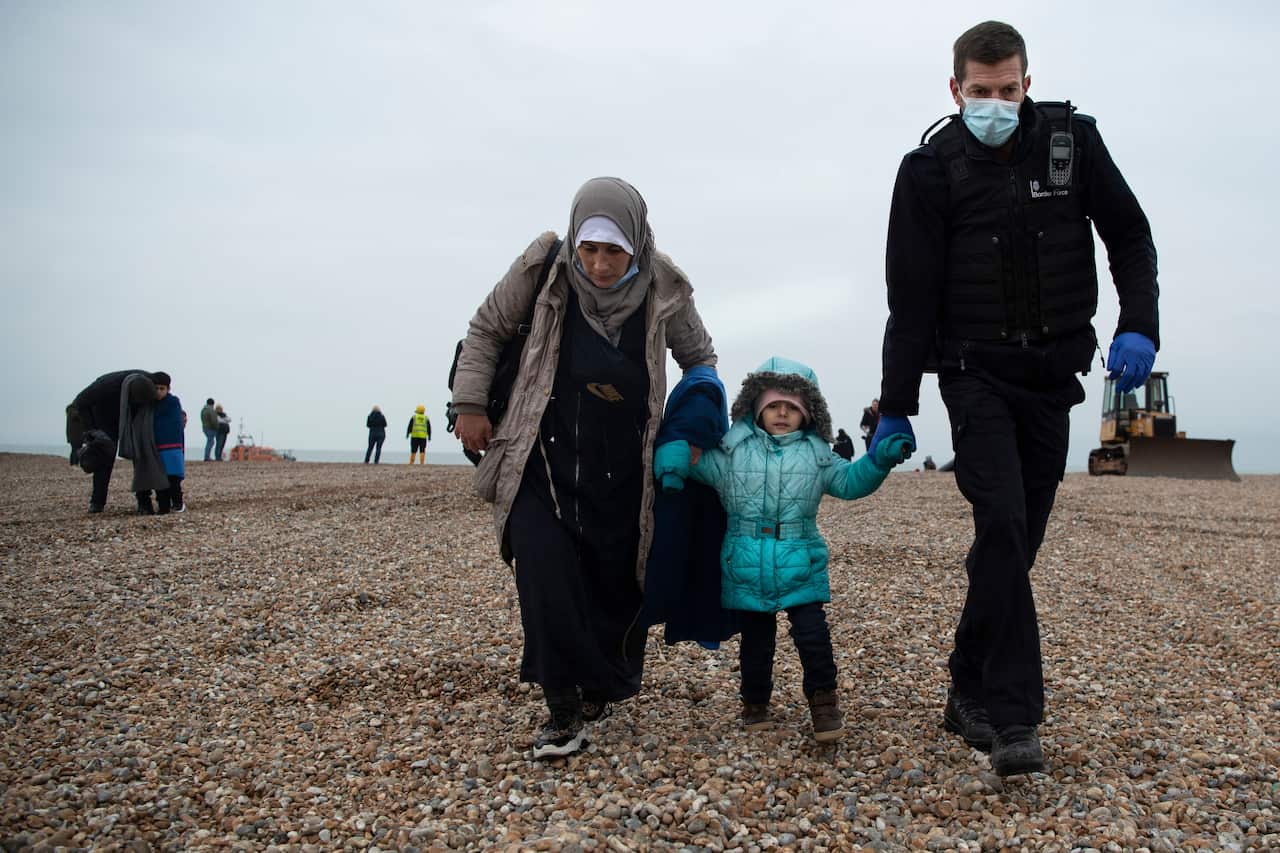 A member of the UK Border Force () helps migrants on a beach in Dungeness on November 24, 2021, after they were rescued while crossing the English Channel. 