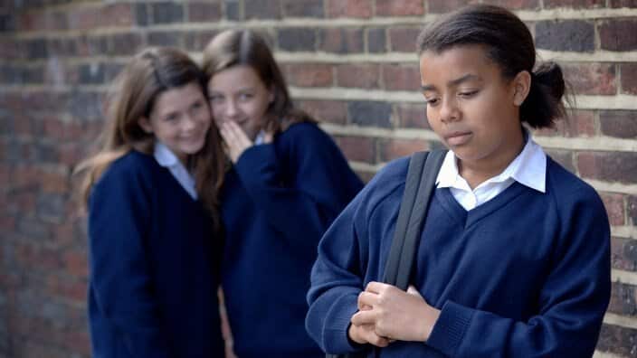 Two school girls whispering and laughing at another girl.