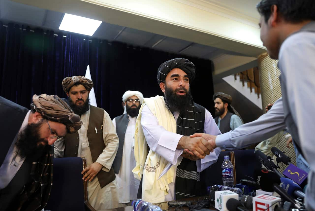 Taliban spokesman Zabihullah Mujahid, centre, shakes hand with journalist after his first news conference, in Kabul, Afghanistan, Tuesday, Aug. 17, 2021.