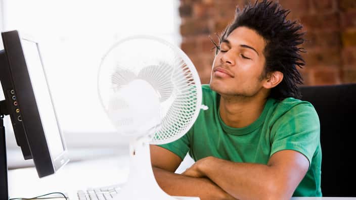 Young man in office with blowing electric fan
