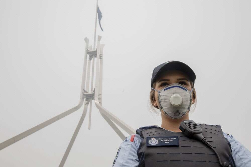 A police officer wears a protection mask while guarding in front of the flag mast on the Parliament House in Canberra