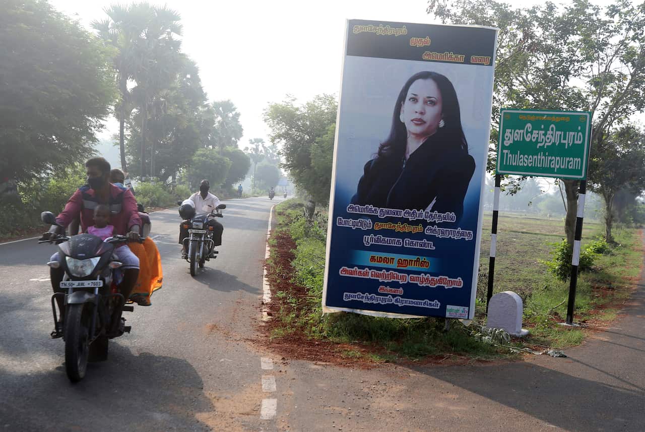 People ride past a billboard featuring US democratic vice presidential candidate Kamala Harris in Thulasendrapuram village, India, Tuesday, 3 November.