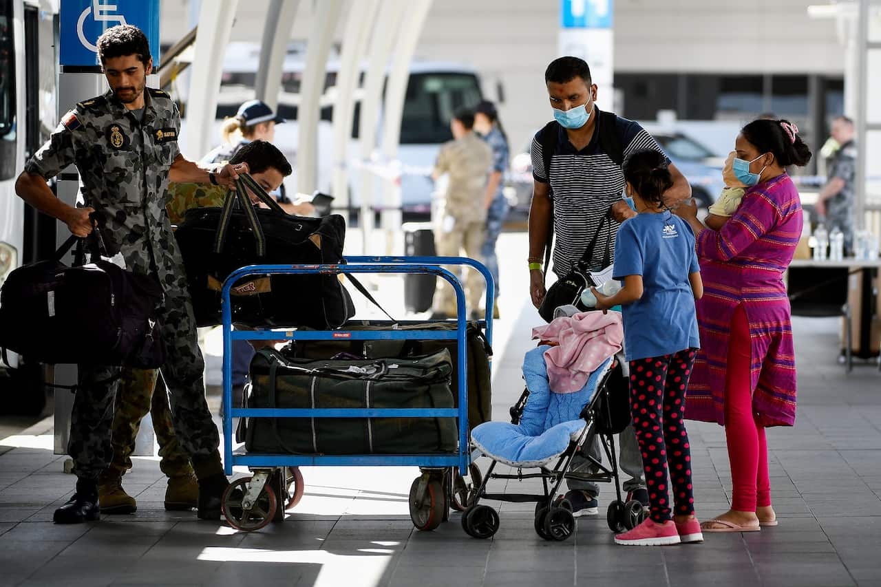 Australian residents returning from India at Sydney International Airport are helped by Royal Australian Navy officers.
