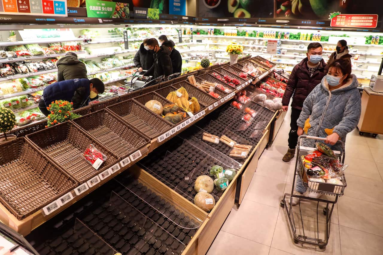 A masked shopper looks at the empty baskets on a counter in a supermarket in Wuhan as locals buy up available food.