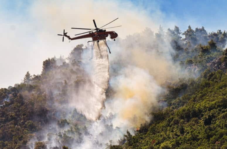 A helicopter drops water over fire in the Thrakomakedones area, in northern Athens, on 7 August, 2021