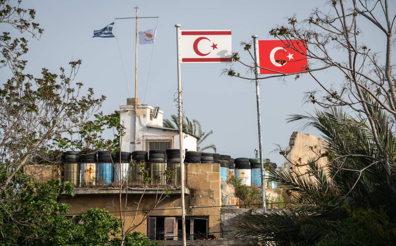 Greek and Cypriot Republic flags in the background. Turkish and Turkish Cypriot flags acoss Cyprus' UN buffer zone