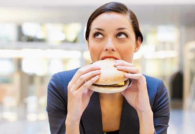 Businesswoman eating hamburger at desk in office