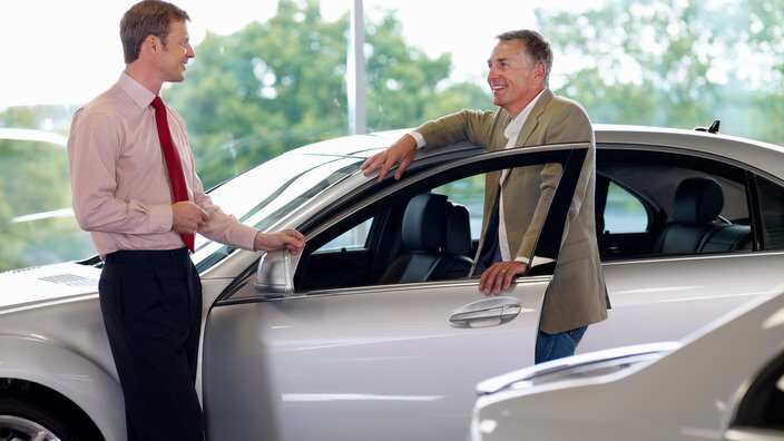 Salesman talking man in automobile showroom