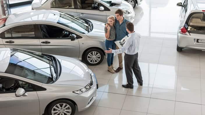 Car dealer showing new car to young couple in showroom