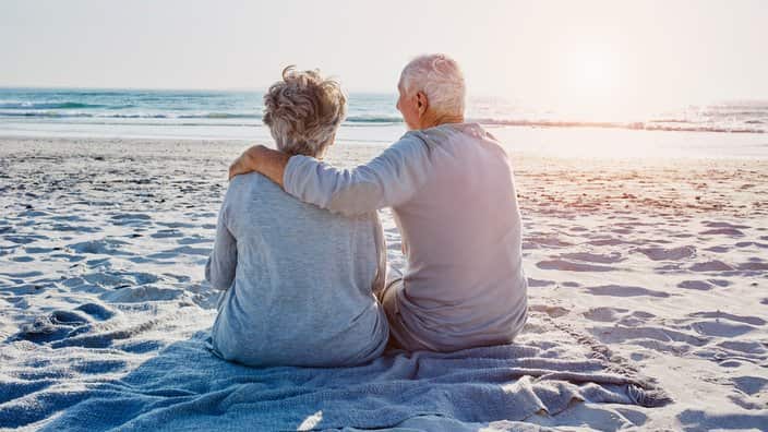 Senior couple sitting on the beach looking at distance