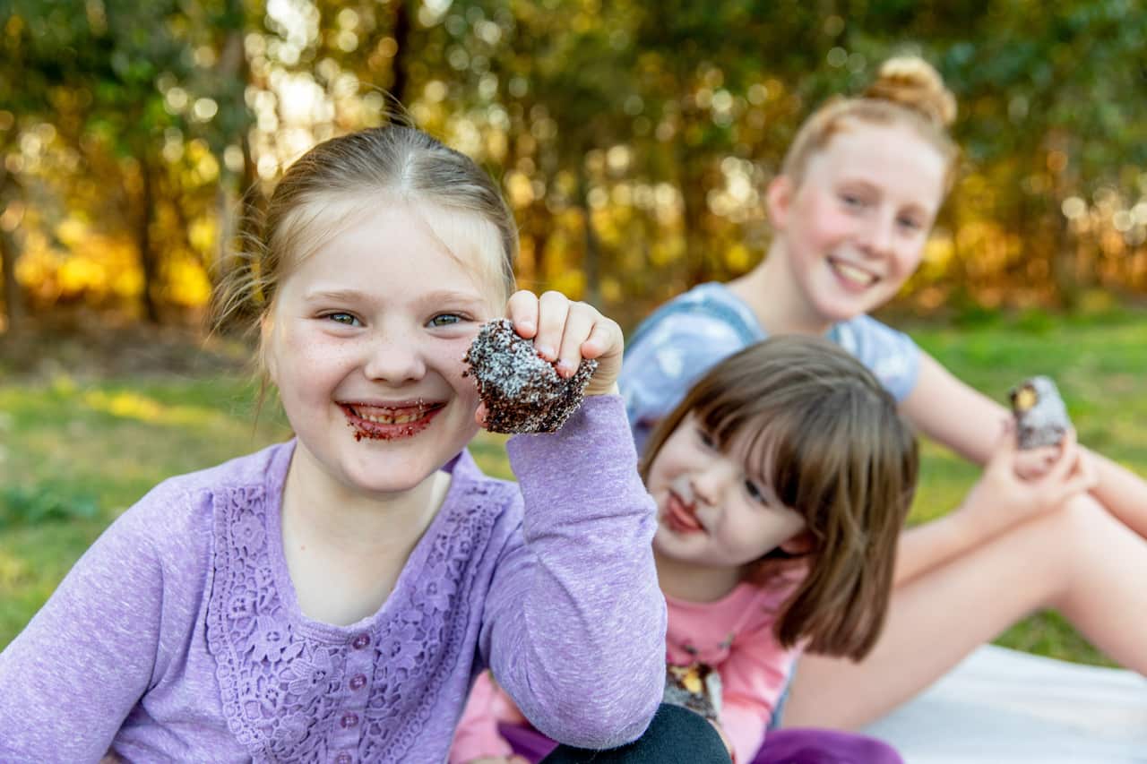 Three young Australian girls hanging out together, laughing and eating lamingtons.