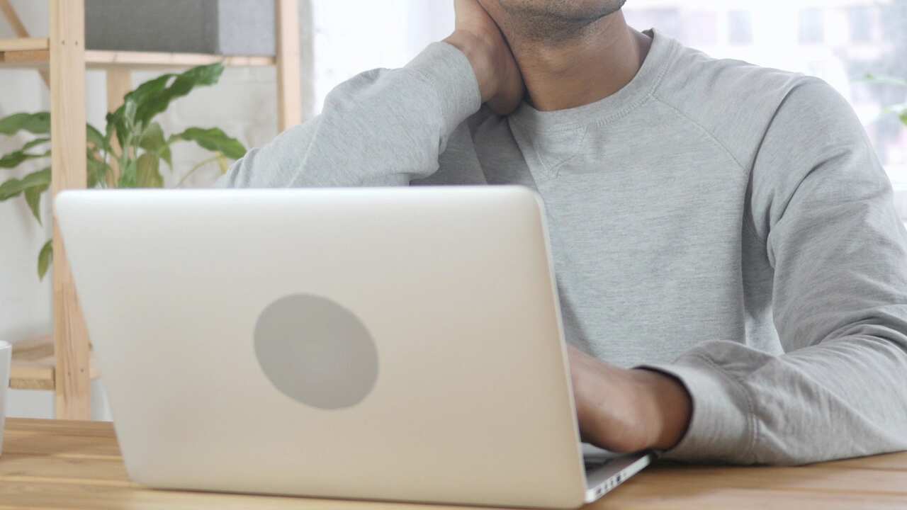 Man with laptop holding neck