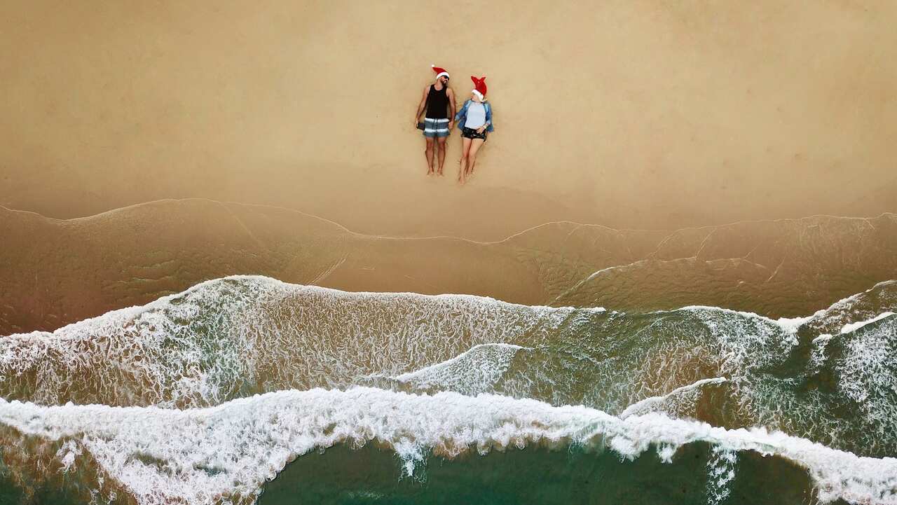 An aerial shot of a young couple sitting on the beach with a Santa hat