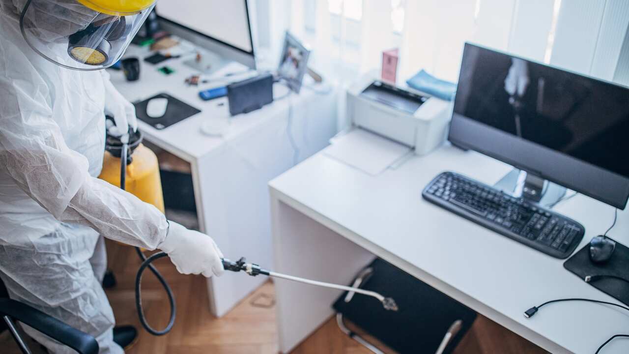 A man in protective suit disinfecting office work space