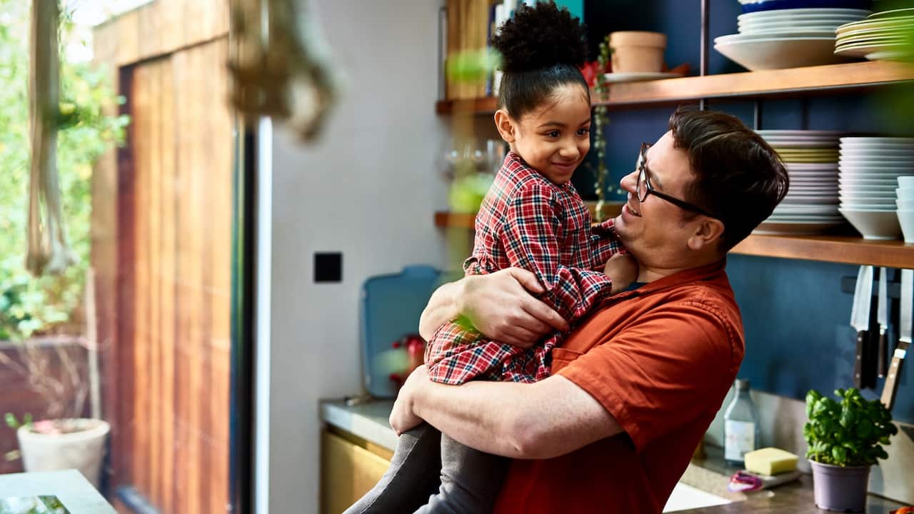 Man holding adopted daughter in kitchen