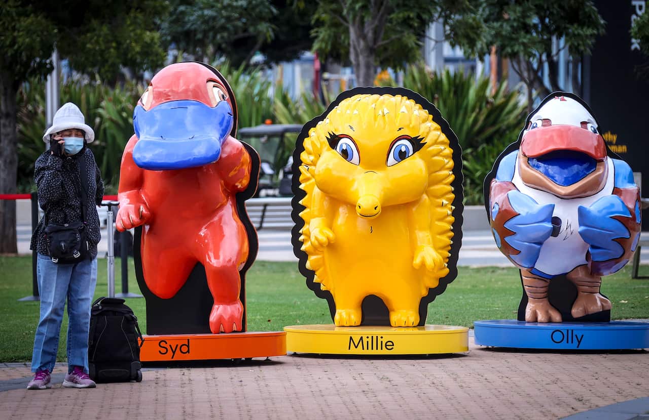 A woman wearing a face mask stands in front of statues of the official mascots for the Sydney 2000 Olympic Games during an event to mark the 20th anniversary of the opening ceremony at Cathy Freeman Park in the Olympic Boulevard in Sydney on September 15,