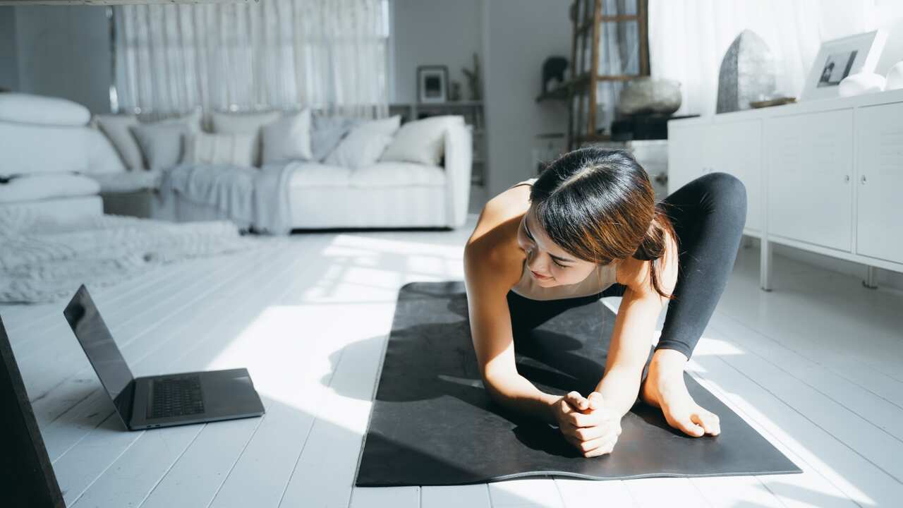 Young Asian woman doing online yoga class with laptop in the living room at home i
