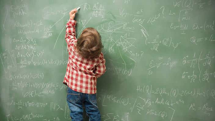 Little boy writing on green blackboard
