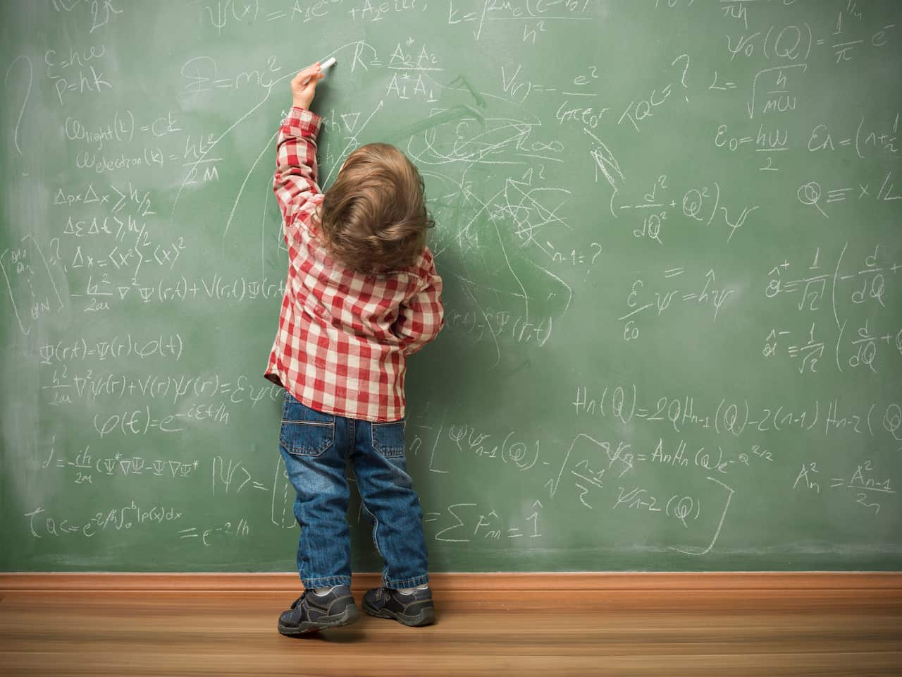 Little boy writing on green blackboard