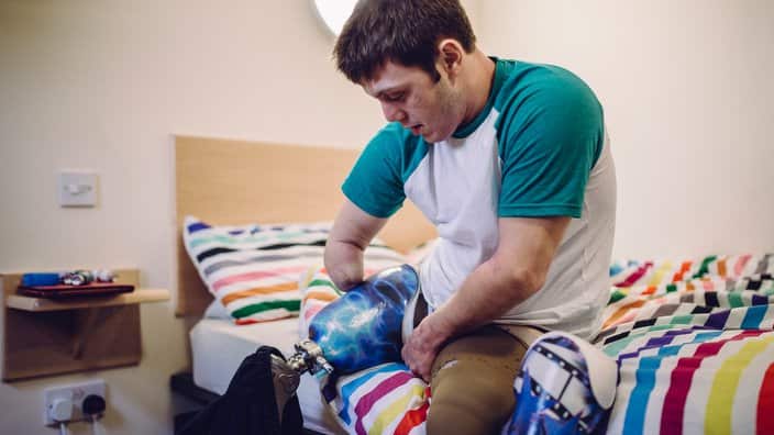 Quadriplegic male putting his prosthetic legs on in his student accomodation.