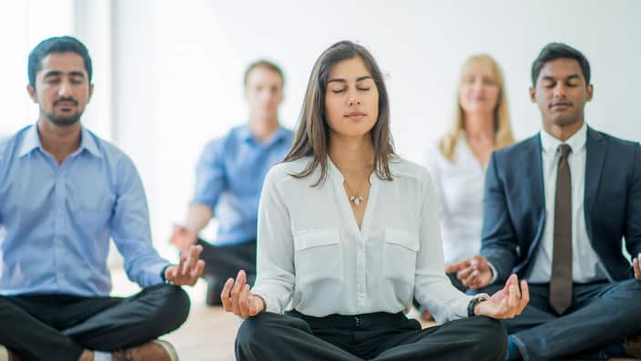 Professional men and women meditating in an office to relax