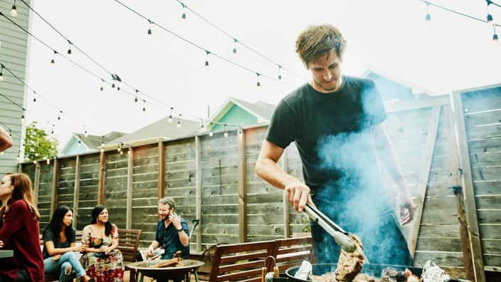 Man grilling steaks for friends at backyard barbecue during party