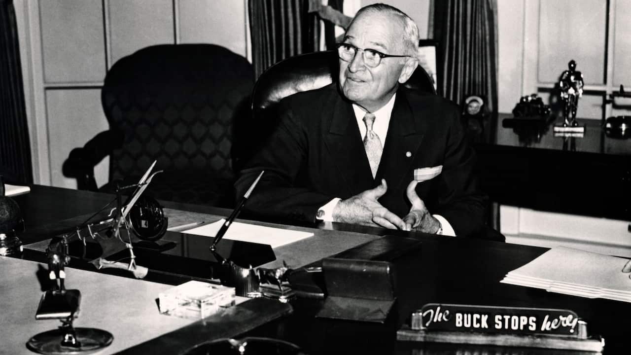 American President Harry S. Truman seated in White House library, with 'The Buck Stops Here' on placard in foreground, circa 1950. 