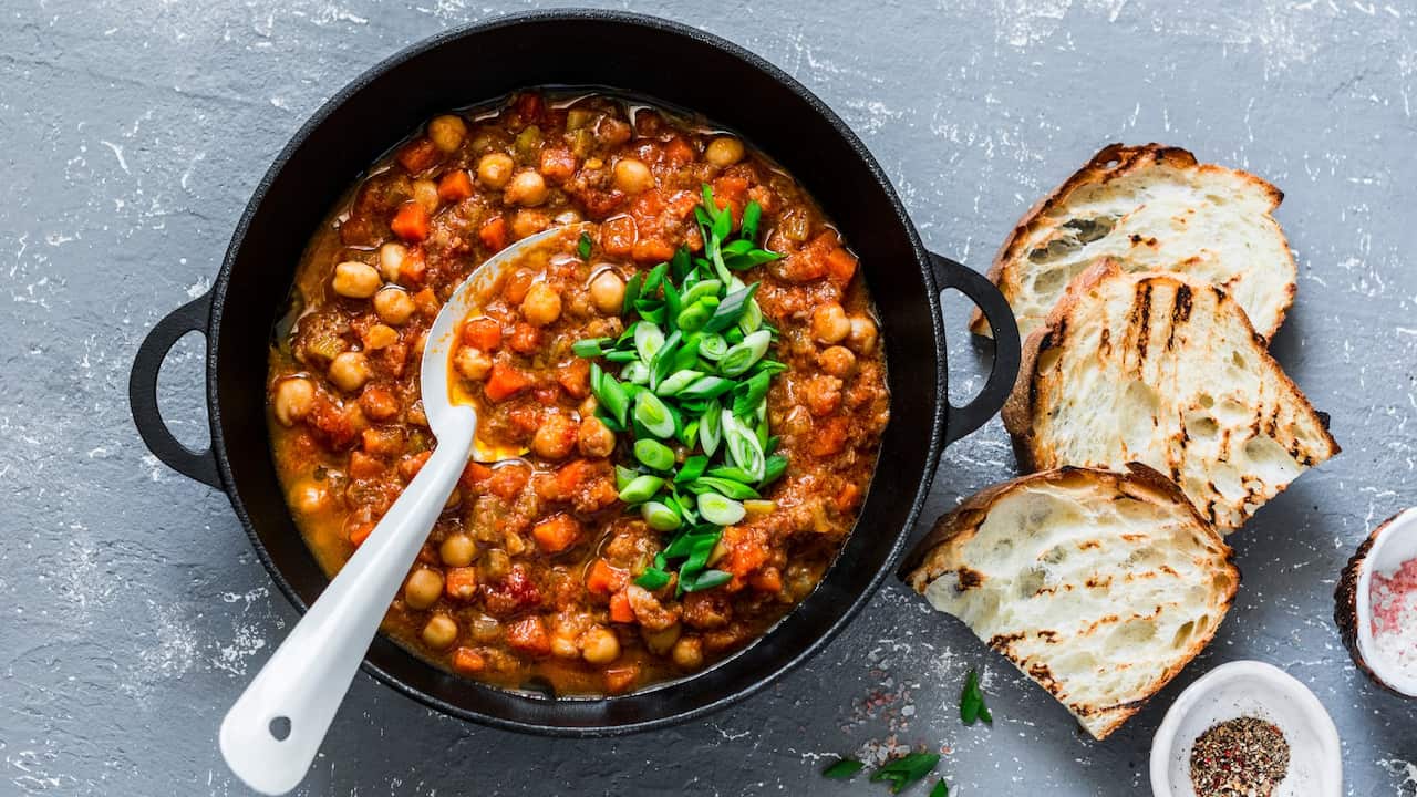 Vegetarian mushrooms chickpea stew in a iron pan and rustic grilled bread on a gray background, top view. Healthy vegetarian food concept. Vegetarian chili