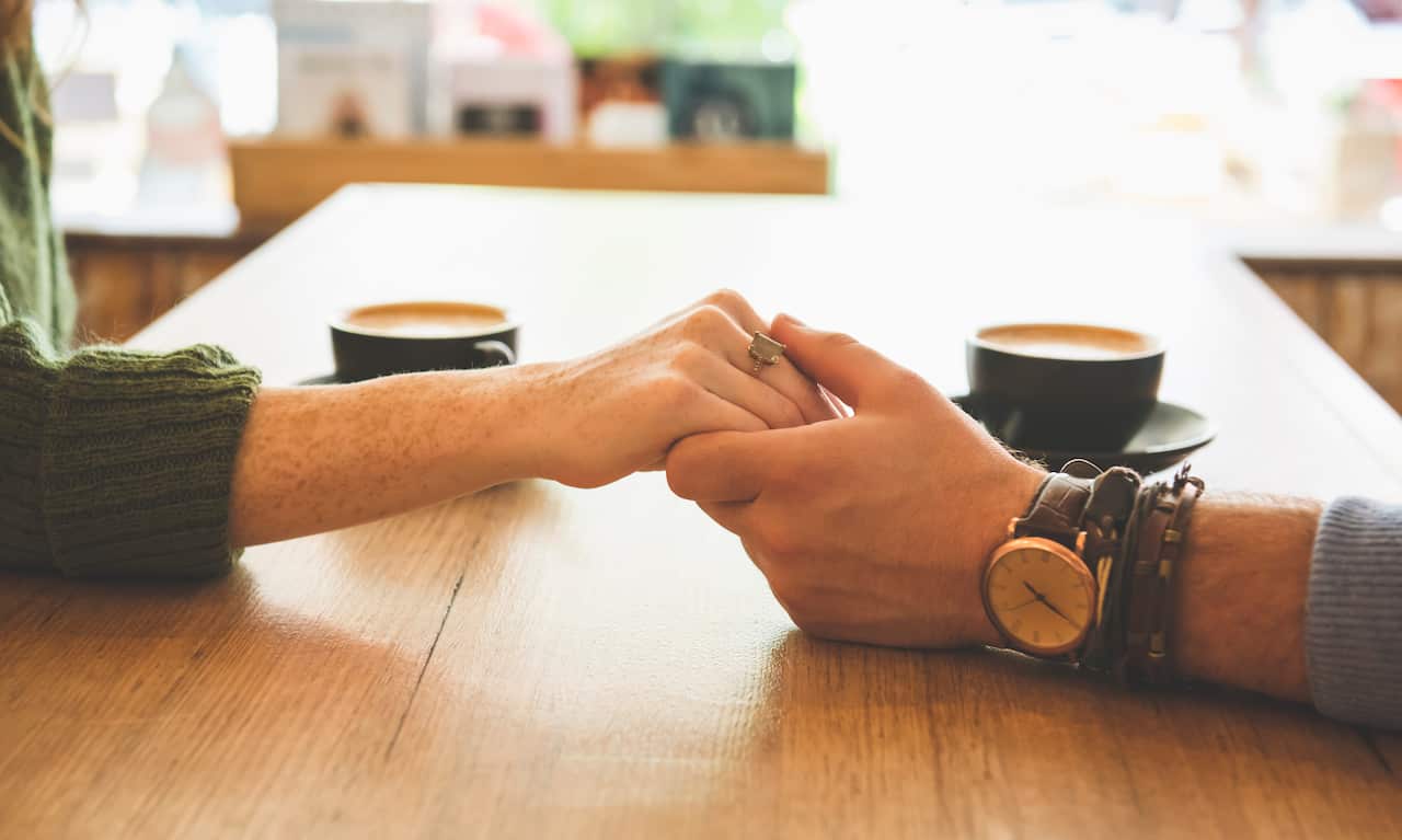 Close up of Caucasian couple holding hands in coffee shop.