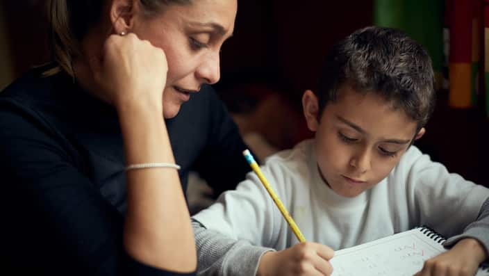 Hispanic mother watching son practicing writing alphabet