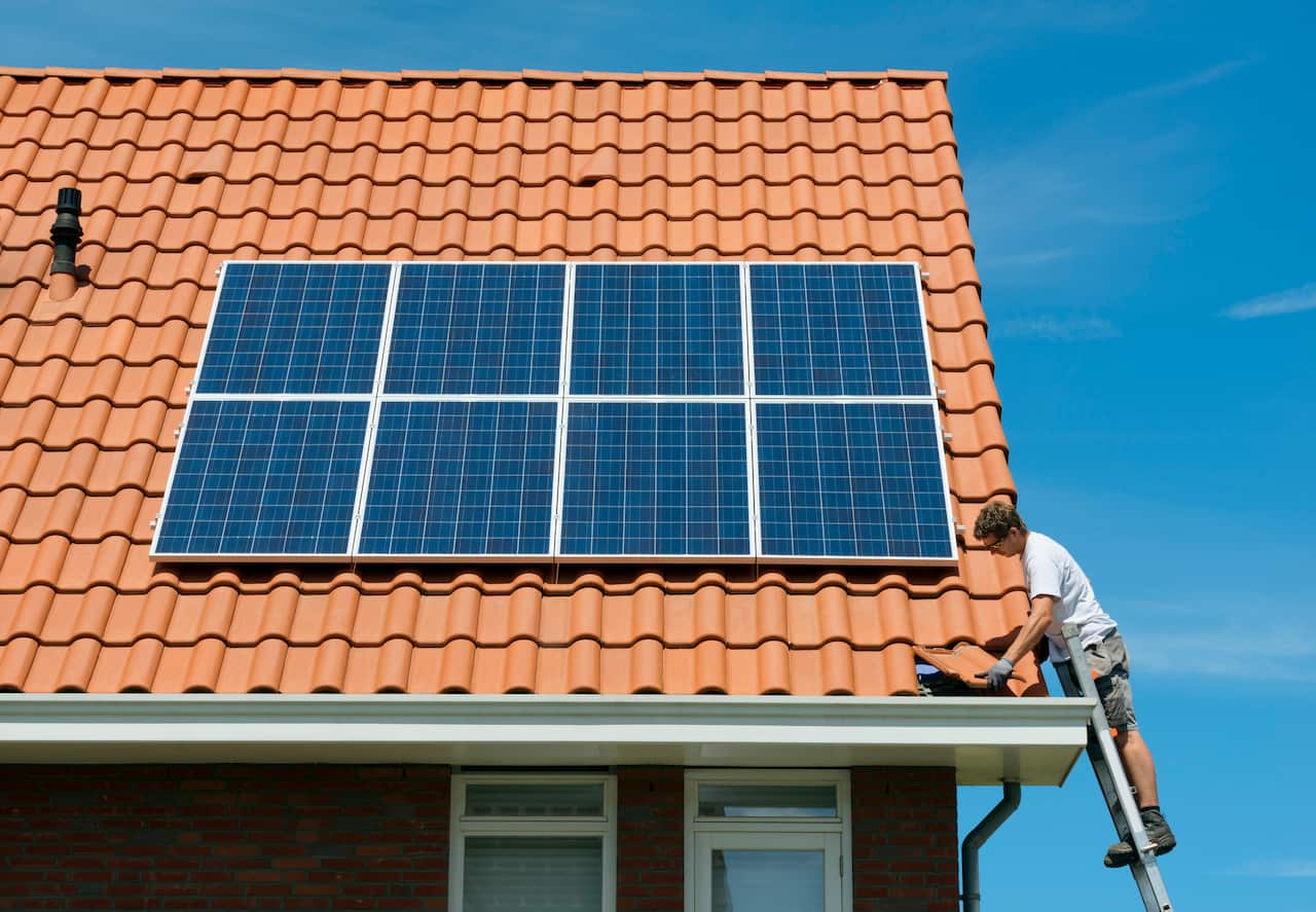 Worker checking installation of solar panels on roof of new home, Netherlands
