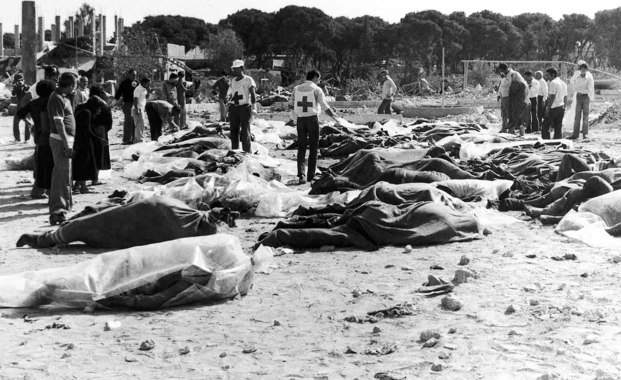 Red Cross and social workers walk among the corpses, on Monday, Sept. 20, 1982, at the Sabra PLO Camp in West Beirut